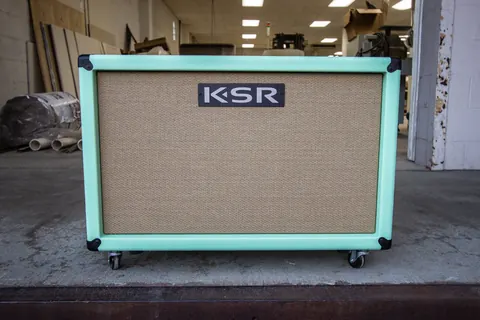 Seafoam green 2&times;12 speaker cabinet on the loading dock, with the shop behind it