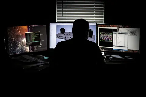 Engineer working across several monitors of circuit and CAD software