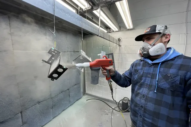 Operator in a respirator powder coating metal parts in the spray booth