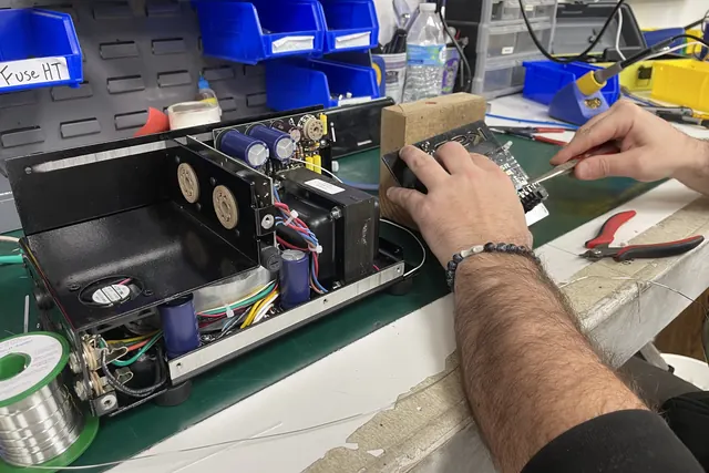 Hands wiring an amplifier chassis on the electronics bench